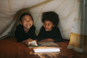 young boy and girl reading a book in a blanket tent